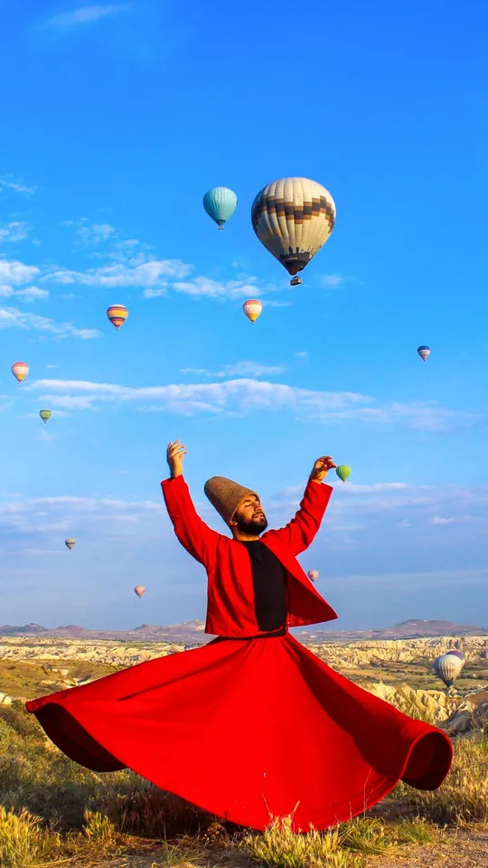 Derviscio rotante in abito rosso che ruota sotto le mongolfiere in Cappadocia